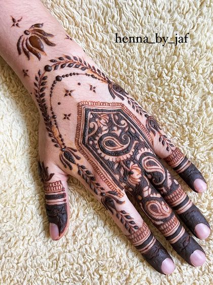 A bold bridal design with a large, filled paisley and geometric shape on the palm. The pattern is framed by a delicate chain of leaves and includes a lotus motif near the wrist.