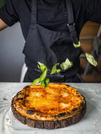A final flourish of fresh basil leaves being scattered over a classic Margherita pizza. It's the details that make a dish perfect.