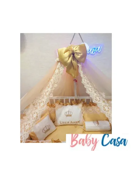 A detailed shot of the "Little Angel" bedding set. The personalized pillows and lace canopy with a large golden bow create a heavenly and opulent space for the baby.