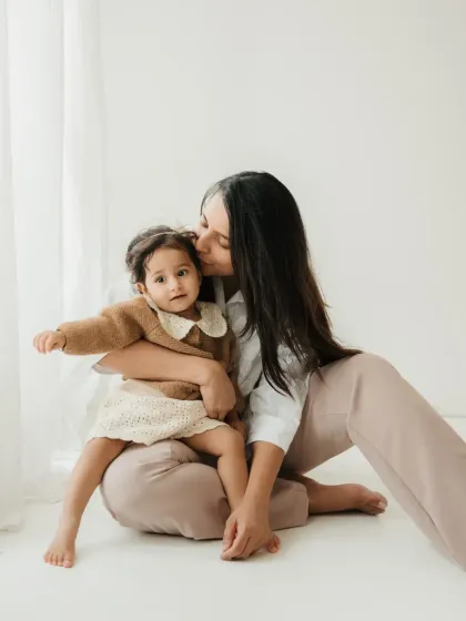 A mother kisses her daughter's head in a simple, elegant studio portrait. The neutral color palette creates a soft and timeless feel.