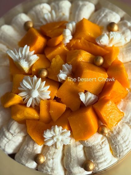 A top-down view of the pull-me-up Mango Cake, decorated with fresh mangoes, edible flowers, and gold pearls.