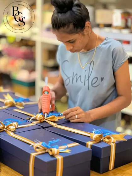 A behind the scenes look at the final touch. Our team member carefully secures a multi-layered gold and blue ribbon onto a navy blue gift box, ensuring every detail is perfect. This is the level of care we bring to every bulk order.