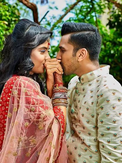 A romantic outdoor portrait of a couple sharing an intimate moment. The lush green background provides a beautiful, natural setting for engagement photos.