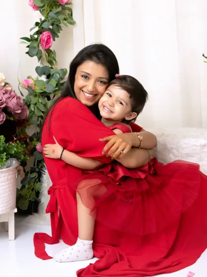 A mother and daughter share a warm, loving hug in their matching red outfits, captured during a special 'Mom and Me' session in my floral-themed studio.