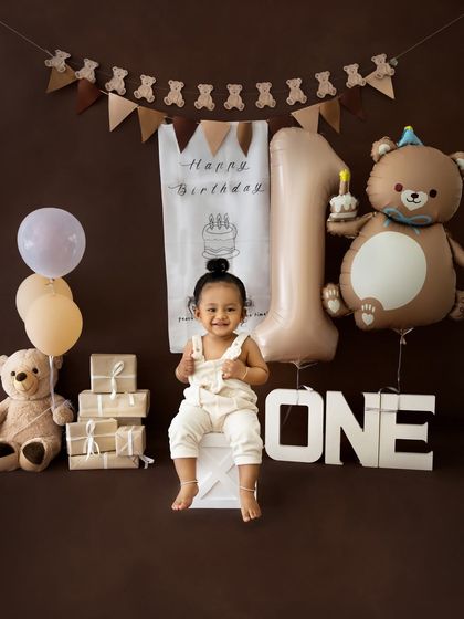 A proud birthday boy sitting on a white block in the middle of his teddy bear themed party setup.