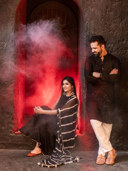 A striking shot using red smoke to create a dramatic and colorful background. The couple's dark traditional outfits stand out beautifully against the vibrant red, making for a memorable image.