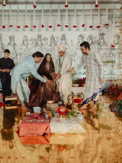 A moment during the wedding ceremony, with the family gathered inside the brass mandap. The golden, reflective floor beautifully mirrors the couple and the intricate decor, adding a layer of surreal beauty to the scene.