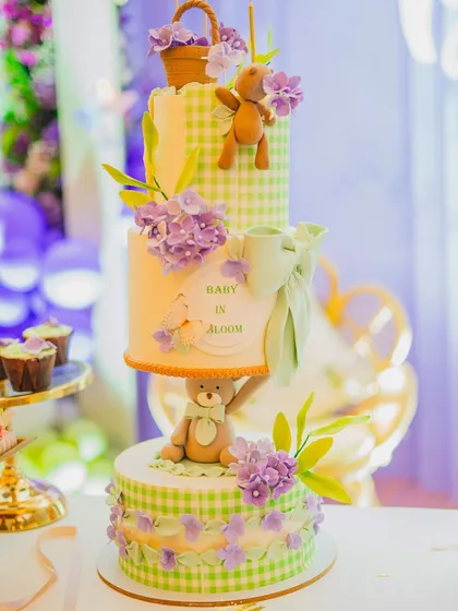 I believe the dessert table should be as beautiful as the main decor. Here, I've styled a stunning multi-tiered 'Baby in Bloom' cake, ensuring it perfectly matches the green gingham and lavender floral theme of the celebration.