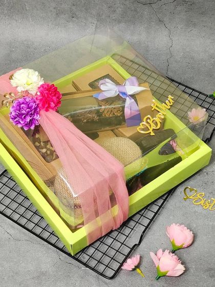 This transparent-lid hamper is beautifully decorated with flowers and ribbons. It's a great way to showcase the delicious brownies and other treats packed inside, perfect for celebrating Raksha Bandhan.