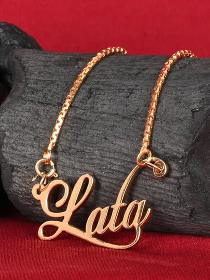 A close-up product shot of a custom nameplate necklace. We use textured backgrounds like this piece of charcoal to create contrast and highlight the jewelry's metallic finish.