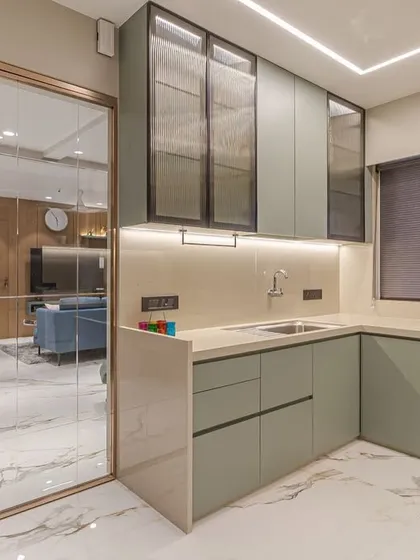 This modern kitchen features custom sage green cabinetry and a functional L-shaped layout. We used fluted glass on the upper cabinets and integrated lighting to create a bright, stylish, and highly practical workspace that opens into the main living area.