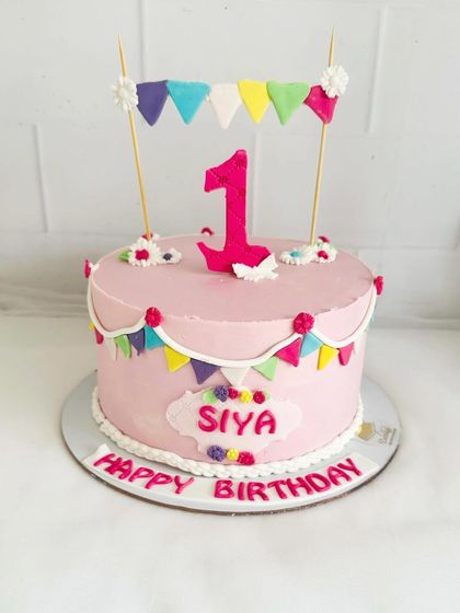 A pretty pink first birthday cake with a colorful bunting design.