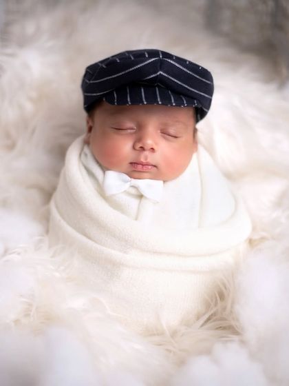 A simple and sweet portrait of the baby swaddled in white with a pinstripe cap, looking peaceful and cozy in the cloud-like setting.