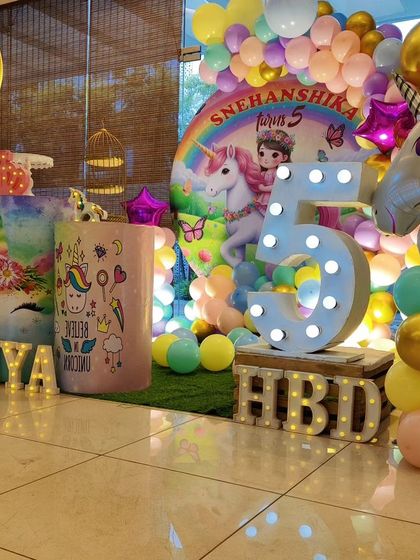 A colorful unicorn-themed fifth birthday. The setup includes a rainbow backdrop, a large unicorn foil balloon, and a 'TIYA' marquee.