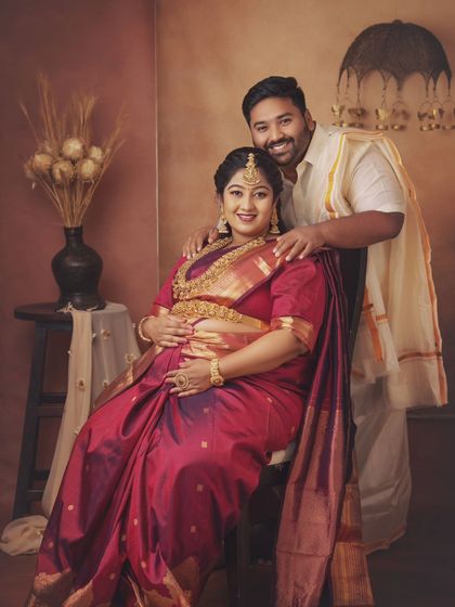 A classic seated portrait of the couple. The dad-to-be stands protectively behind his wife, their pose reflecting their partnership and shared joy.