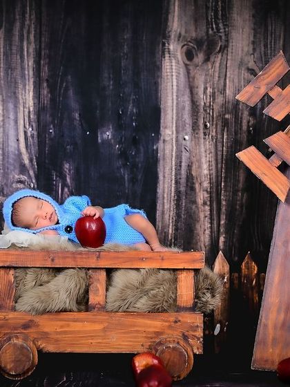 A newborn rests peacefully in a rustic wooden cart. This setup combines natural textures with the baby's soft features for a beautiful contrast.