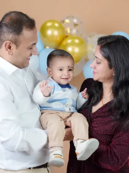 A candid moment of interaction during a first birthday family shoot. The parents look on with love as their little one smiles, creating a natural and heartwarming family portrait.