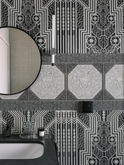 This black and white bathroom is a cozy haven. The intricate art-deco style wallpaper and tiles create a warm, enveloping feeling, perfect for a relaxing soak.