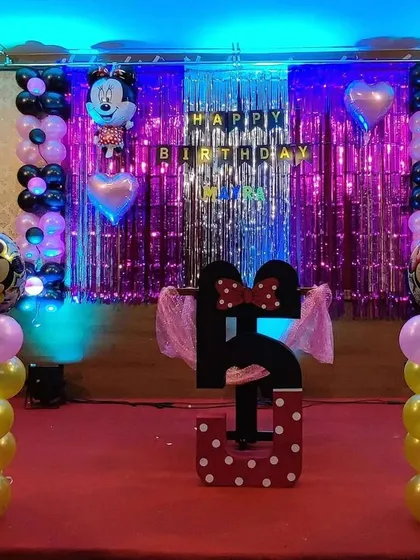 A classic Minnie Mouse themed party for a fifth birthday. This setup uses Minnie's iconic colors with pink and yellow balloon columns, a large number "5" cutout, and Mickey and Minnie foil balloons against a shimmering backdrop.