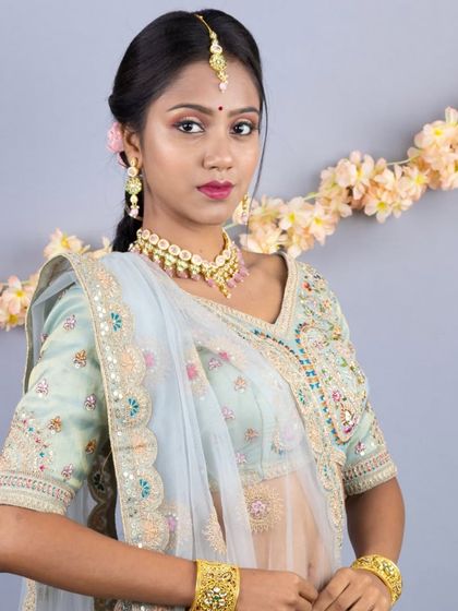 A close-up portrait showing the delicate jewellery and the intricate embroidery on the blouse of the peacock-themed lehenga.