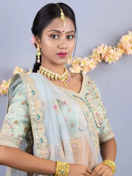 A close-up portrait showing the delicate jewellery and the intricate embroidery on the blouse of the peacock-themed lehenga.