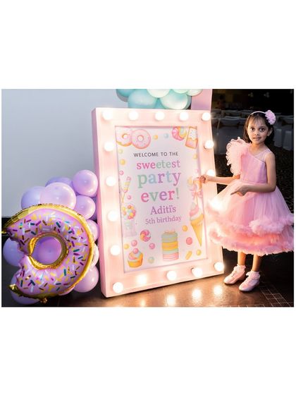 A 'Sweetest Party Ever' welcome sign with marquee lights. The birthday girl stands beside it, next to a giant donut-shaped balloon.
