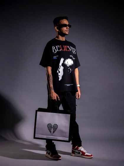 A full-length studio shot of a male model in an oversized graphic tee and sneakers, holding a branded bag. This is a complete look that's perfect for a lookbook, showing how different brand items can be styled together.