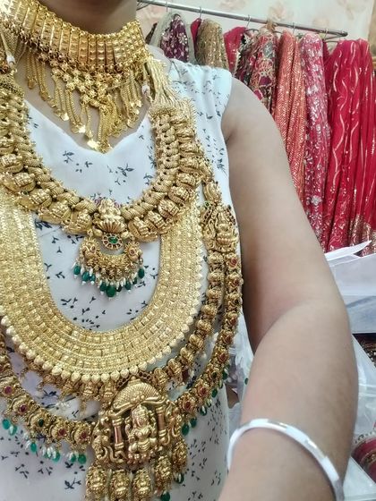 A person trying on a heavy South Indian temple jewellery set, showing the scale and grandeur of the pieces.