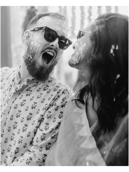 A playful, candid moment from Ben and Shrutika's Haldi. The black and white image focuses on their expressions, capturing the fun and slightly chaotic energy of the ritual.