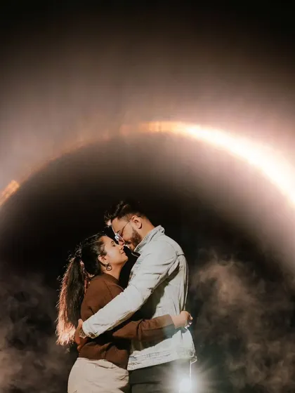 A couple is framed by a ring of light in a smoky, dark room, creating a futuristic and moody portrait. This is a great example of our creative and conceptual pre-wedding photography.