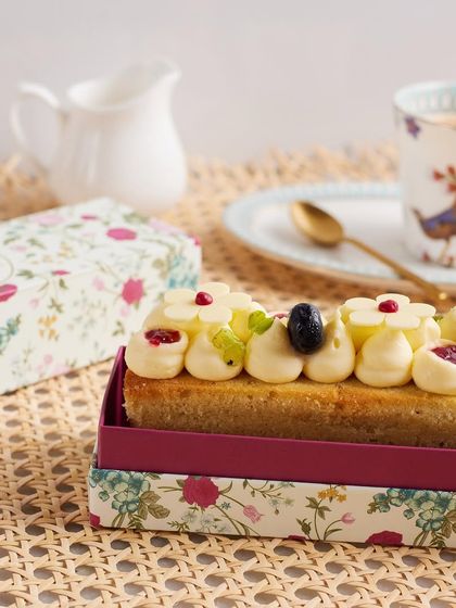 A slice of elegance. This teacake, topped with blooms and berries, is shown with its beautiful floral packaging, perfect for an evening treat.