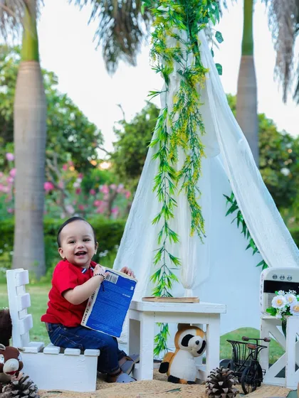 A happy one-year-old boy enjoys an outdoor picnic-themed shoot, laughing as he plays with a book in the fresh air.
