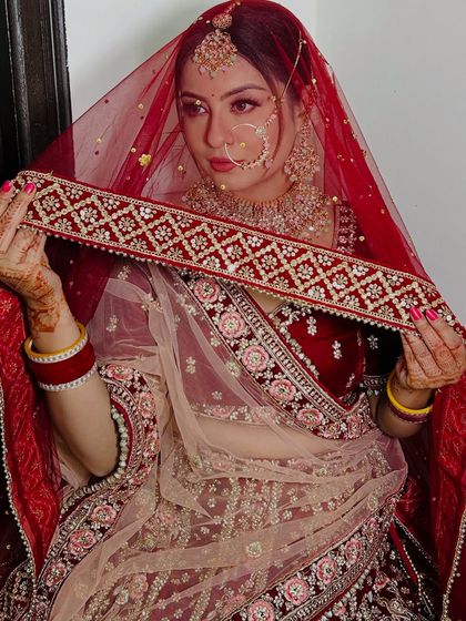 The bride showcasing her full lehenga and dupatta. The makeup is designed to complement the rich velvet and detailed embroidery of her outfit.