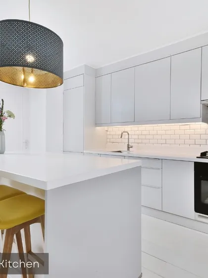 A showcase of a modern, all-white modular kitchen with a functional island that doubles as a breakfast counter. The design emphasizes a clean aesthetic with handleless cabinets, subway tile backsplash, and under-cabinet lighting for a bright, efficient cooking space.