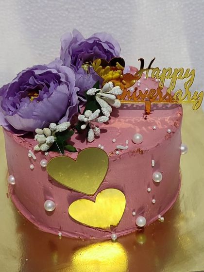 A mini anniversary cake in a lovely mauve color, decorated with purple flowers and golden hearts.