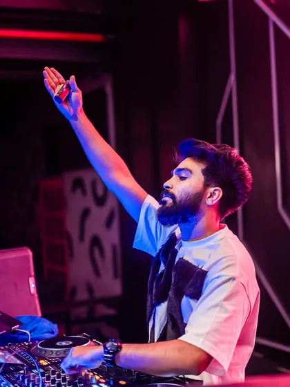 Hand in the air, feeling the beat. This is a classic DJ pose that captures the energy of the moment.