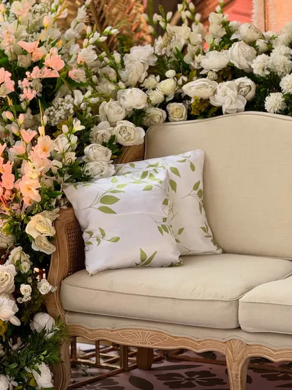 A close-up of a classic caned sofa, nestled in a corner of lush white and pink flowers. This demonstrates our belief that seating should be both comfortable and beautiful.
