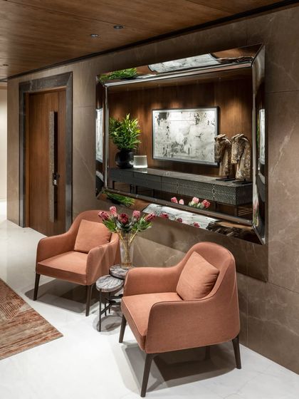 A cozy seating nook in the Camellias lobby, featuring two armchairs in a warm terracotta hue. A large mirror reflects a pyrite-inlaid sideboard, creating a dialogue between restraint and richness.