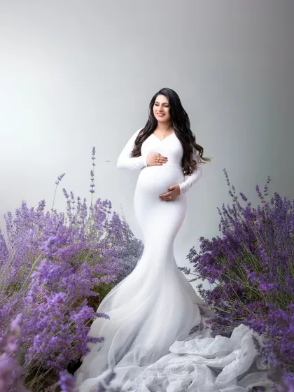 Serenity among the lavender. We created a field of lavender in our studio for this peaceful portrait. The mother-to-be, in a classic white gown, looks serene and beautiful, surrounded by the calming purple hues.