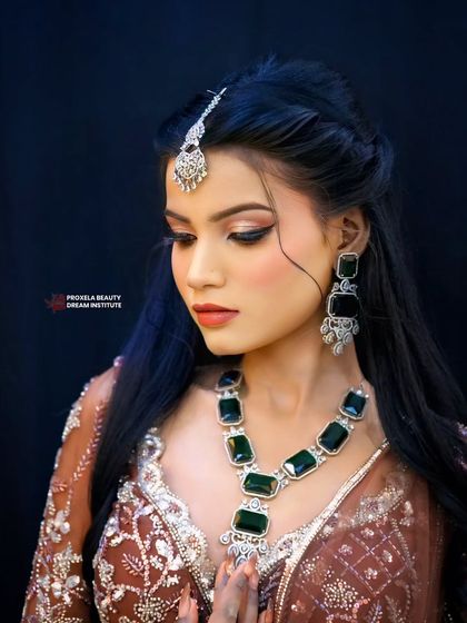 A glamorous look for any festive occasion. The hair is styled in a half updo with soft waves, beautifully framing the face and showcasing the statement emerald green necklace.