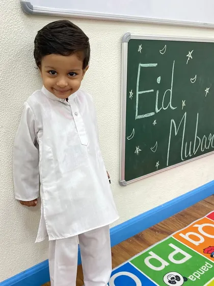 Eid Mubarak. This little boy looks charming in his white kurta, standing by the classroom blackboard decorated for the Eid celebration.