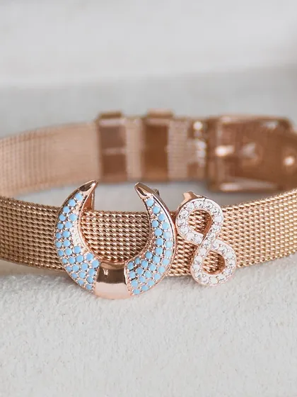 A close-up of a custom watchbelt bracelet, featuring a crescent moon and an infinity charm.