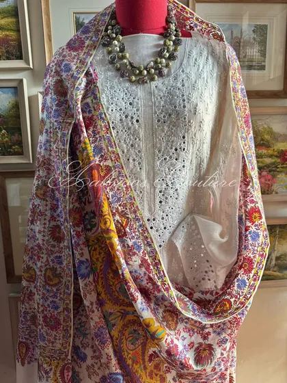 We celebrate a vibrant fusion of crafts with this ensemble. A pristine white Chikankari suit, detailed with delicate mirrorwork, is paired with a colorful Kashmiri Kalamkari dupatta, showcasing a symphony of floral and paisley motifs.