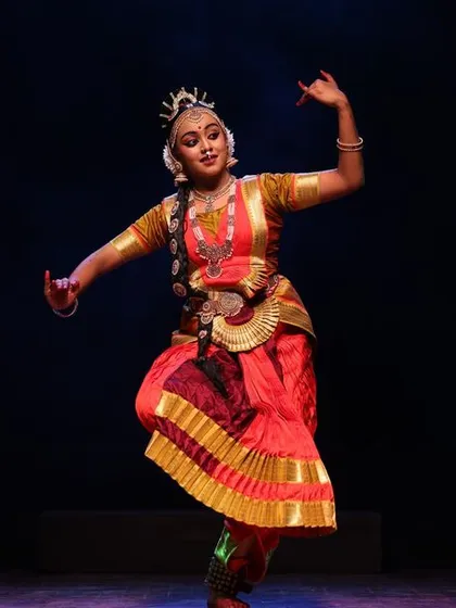 A solo dancer in a striking pose, her form beautifully illuminated against the dark stage at the Sadhana festival.