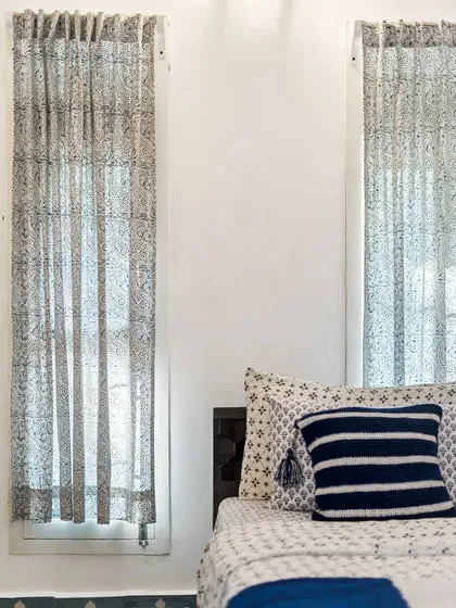 A close-up of the bedroom, focusing on the delicate, block-printed sheer curtains that filter the natural light beautifully. The detail highlights the craftsmanship and textile choices in the room's design.