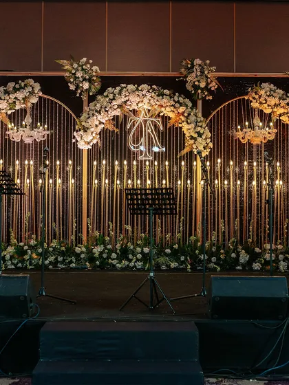 For a modern and chic Sangeet or reception, we designed this stunning stage featuring a wall of warm candle lights, elegant floral arches, and a personalized neon monogram for the couple.