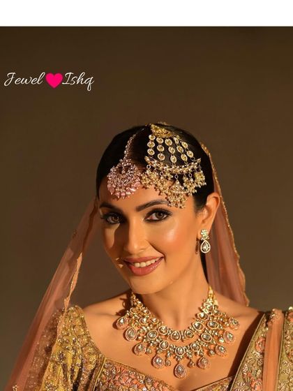 A smiling bride showing off her complete head jewellery, featuring a pink-stoned maang tikka and a multi-layered passa.