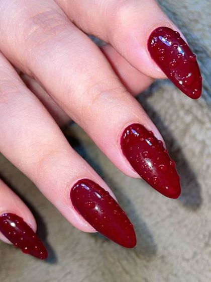 A bold and dramatic look. These long, stiletto nails are painted in a deep, glossy red and feature a unique 3D water droplet effect for a touch of avant-garde style.