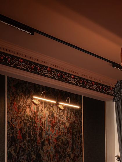 The custom cornice detail in its final context, sitting above a textured wallpaper panel. The integrated picture light illuminates the wall below, while the cornice itself acts as a decorative crown, finishing the room with intention and elegance.