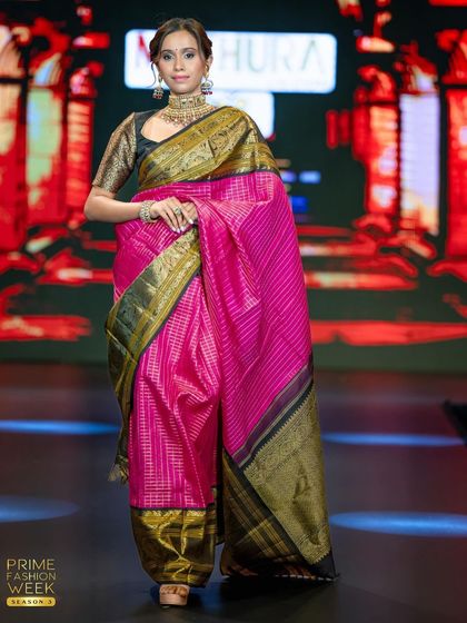 This model showcases a vibrant pink Kanchipuram silk saree with a contrasting black and gold border, a bold and beautiful statement piece.